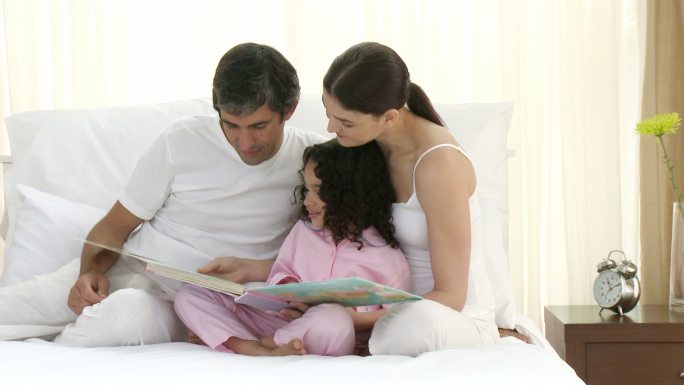 父母和女儿一起在床上看书特写