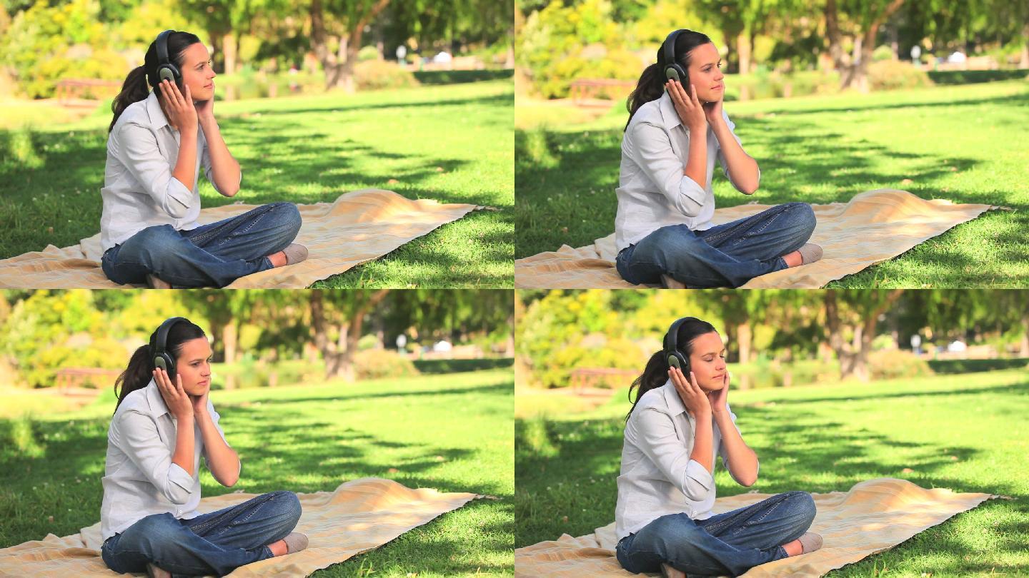 女人坐在公园的草地上听音乐