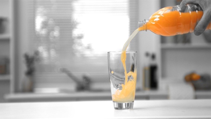 在黑白慢镜头中，一名男子用手将一瓶橙汁倒入玻璃杯中