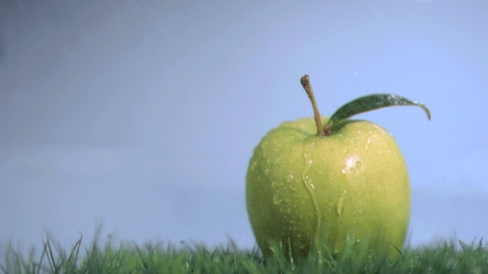 在蓝色背景下，苹果在草地上被打湿的慢镜头