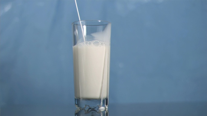 牛奶倒入玻璃杯慢镜头，在蓝色背景下