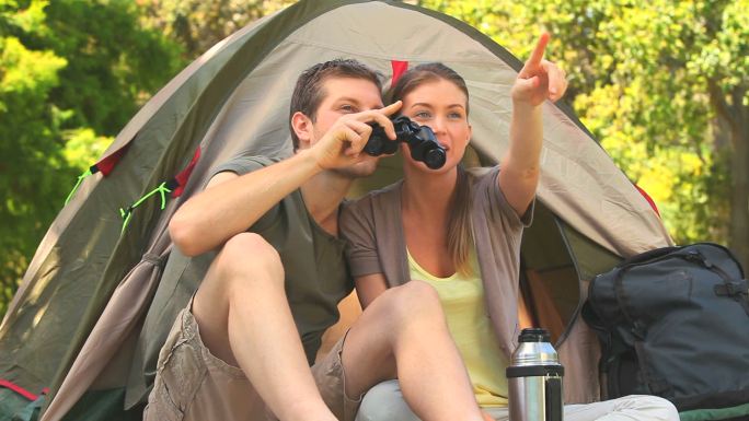 一对夫妇坐在帐篷外用双筒望远镜