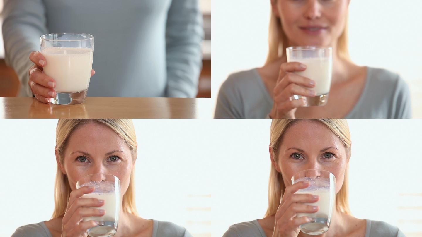 一个女人从桌子上拿起一杯牛奶，喝了一口