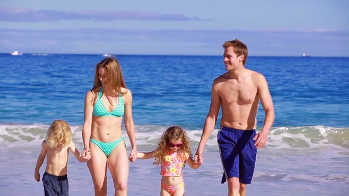 幸福的一家人在海滩上牵着手散步