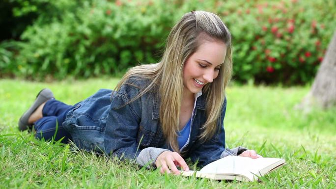一个白人金发少女趴在草地看书