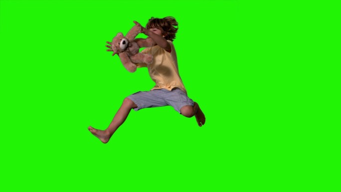 在慢镜头中，小男孩跳起来抓住绿色屏幕上的泰迪熊