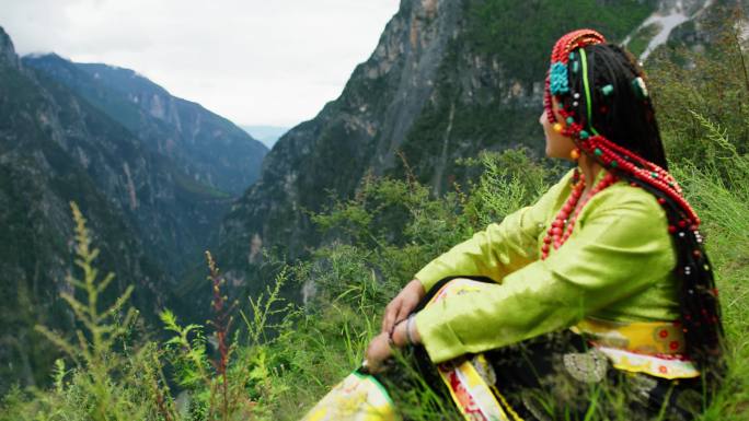 藏族女子坐在草地上欣赏高山风景