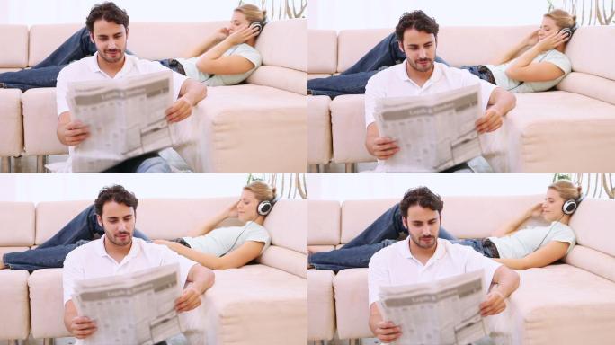 男人在看报纸，而他的女朋友在客厅听音乐