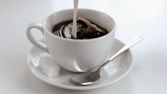 牛奶在白色背景下以超慢的动作滴在咖啡杯里