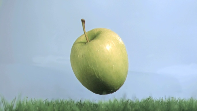绿苹果在蓝色背景下以超慢的动作落在草地上