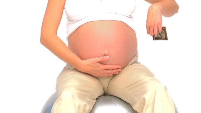 一名怀孕女性在健身球上拿着她未来宝宝的扫描图