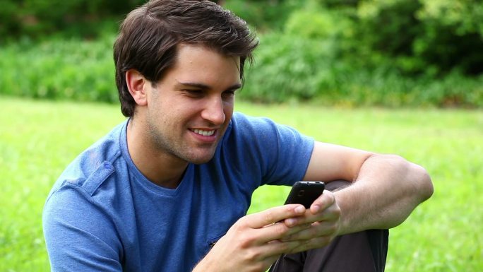 在公园里用手机打字的微笑男人