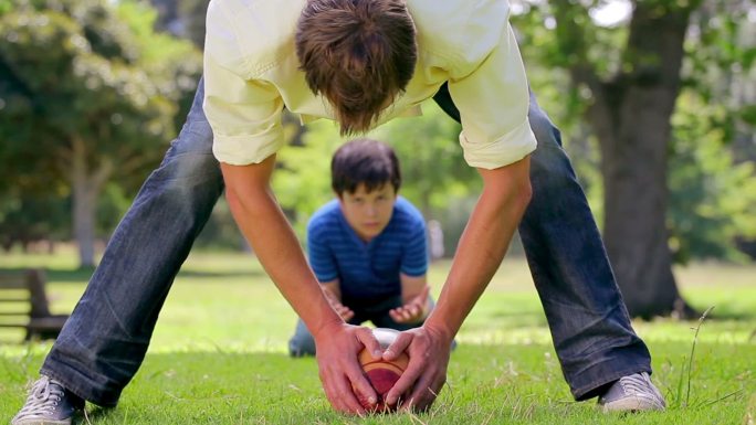 微笑的男人和他的儿子在乡下玩橄榄球