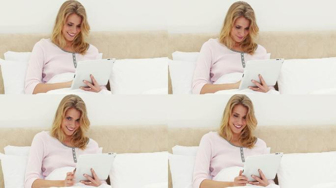 微笑的金发女人在她的卧室里使用电子书