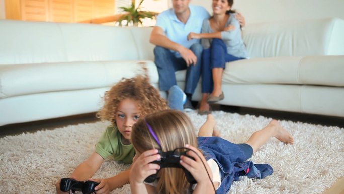 孩子们在地毯上玩电子游戏，而他们的父母在观看