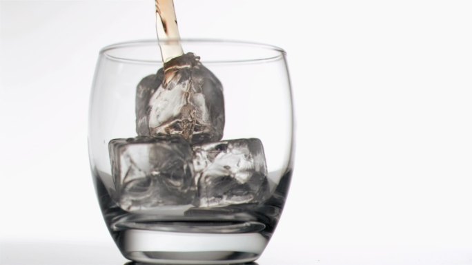 威士忌以超慢动作倒入加冰的玻璃杯中