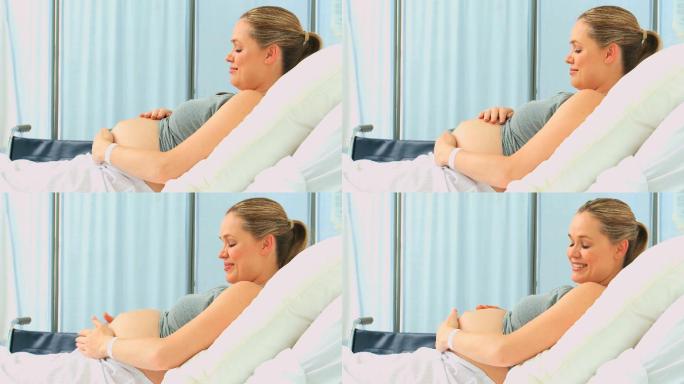 一名孕妇在诊所的床上摸着自己的肚子