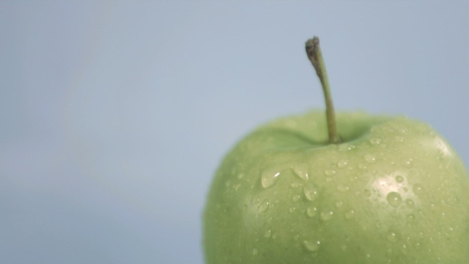一个带水滴的青苹果慢镜头，在灰色背景下