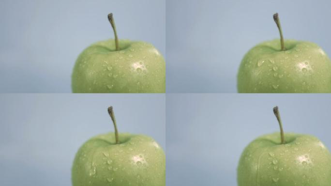 一个带水滴的青苹果慢镜头，在灰色背景下