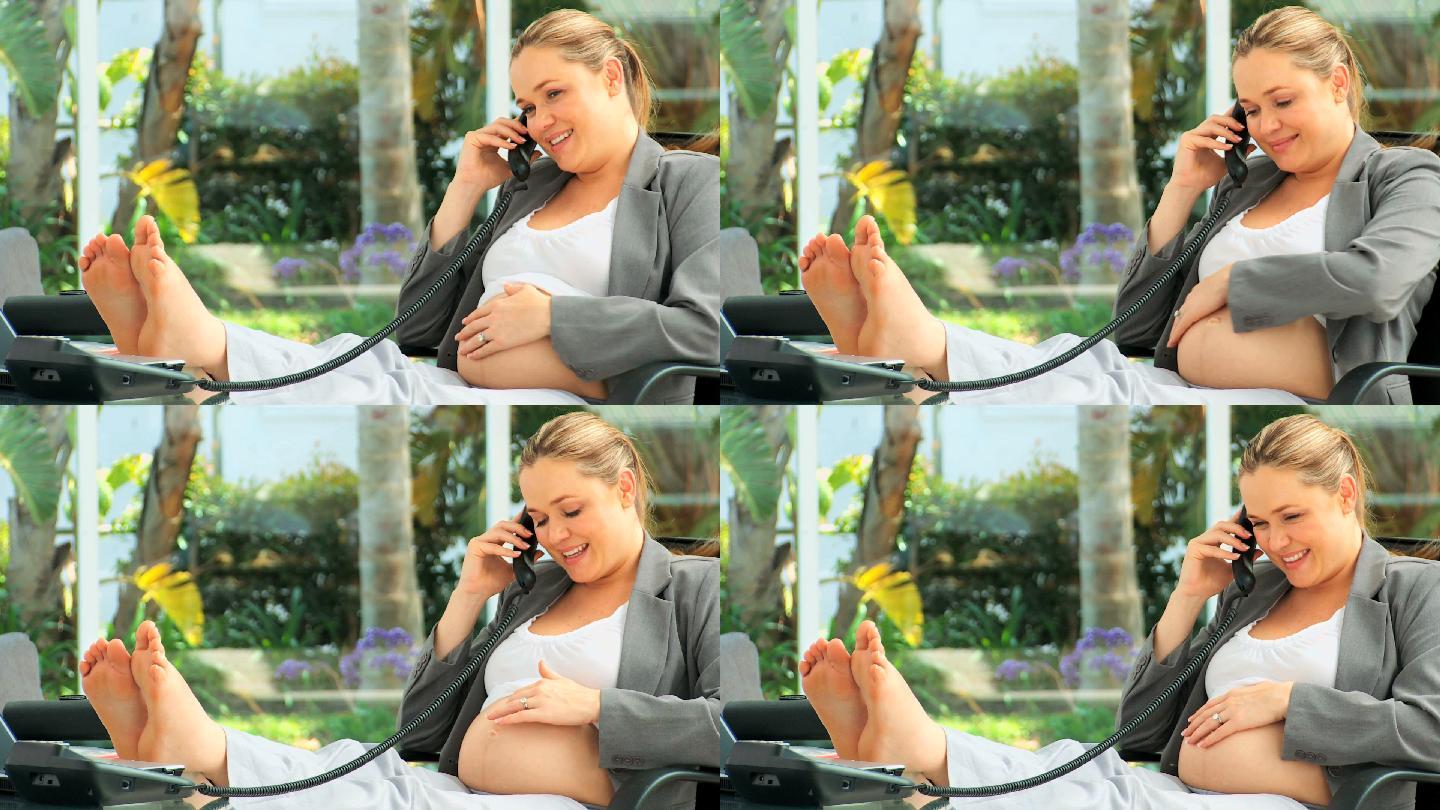 放松的孕妇在她的桌子上讲电话