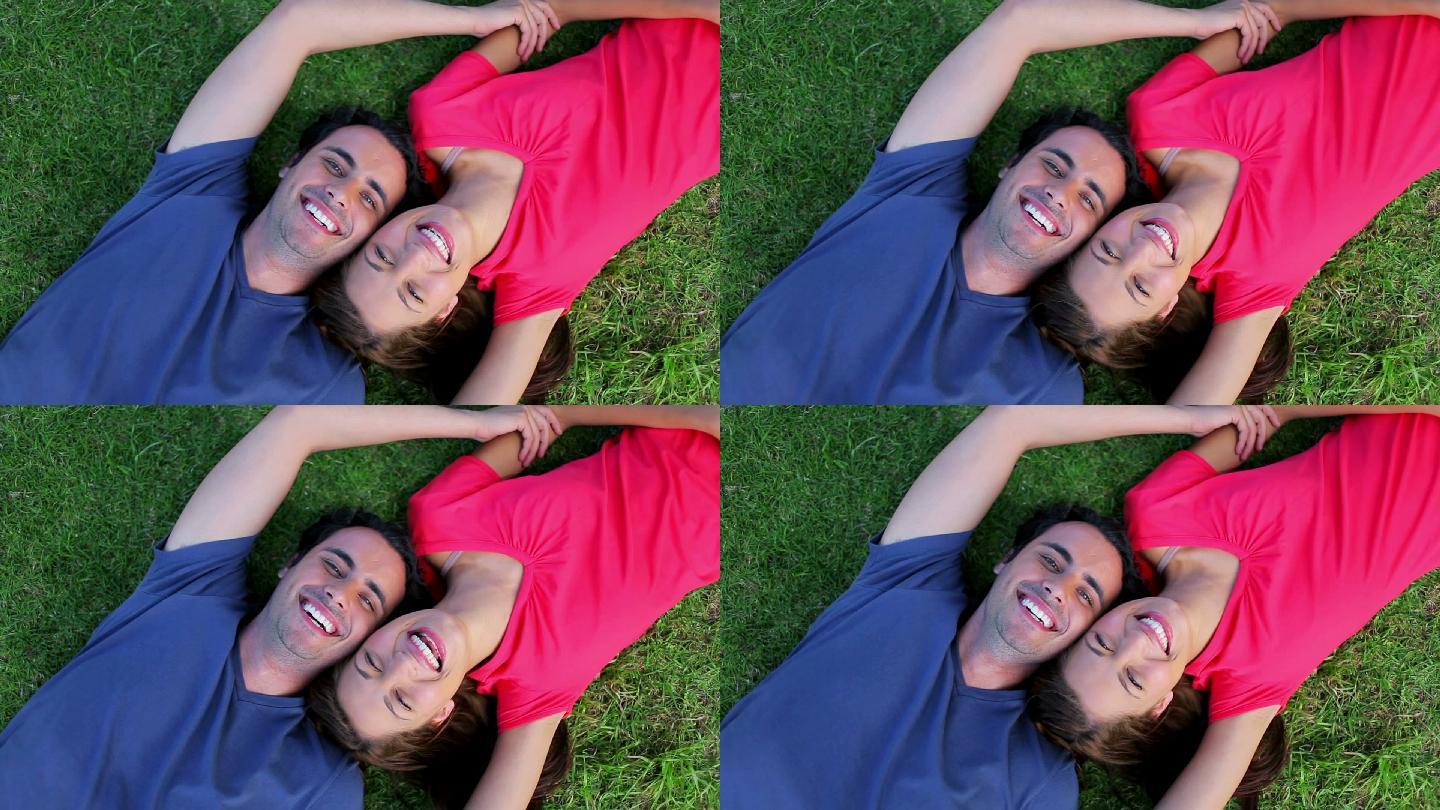一对微笑的情侣躺在草地上，在公园里享受大自然