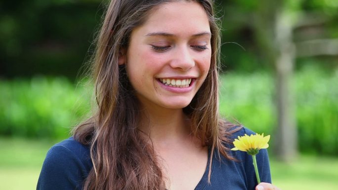 微笑的年轻女子闻着公园里的一朵花