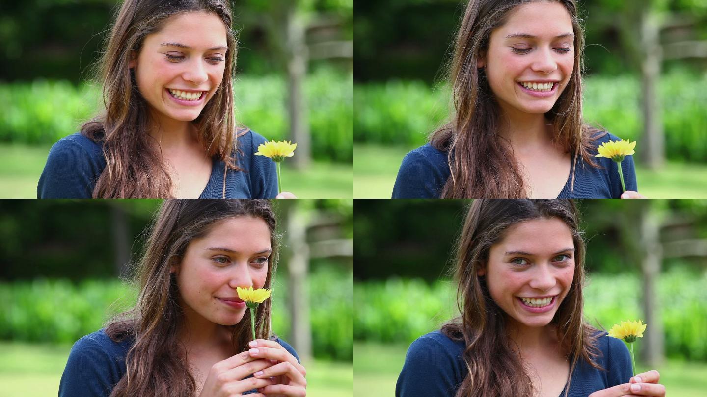 微笑的年轻女子闻着公园里的一朵花
