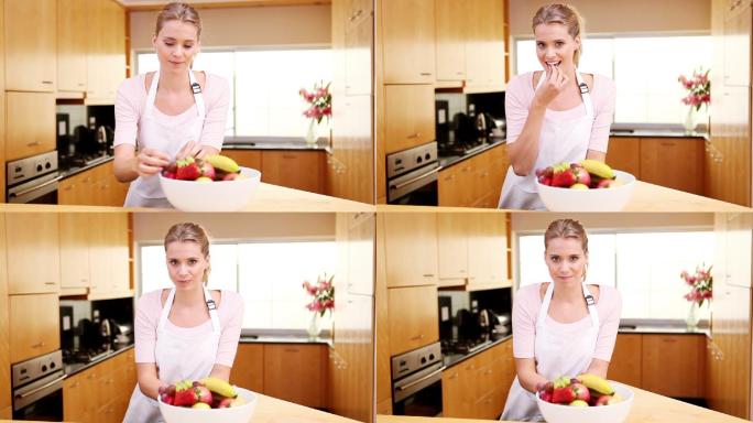 一个年轻的女人把一碗水果放在厨房的工作台上