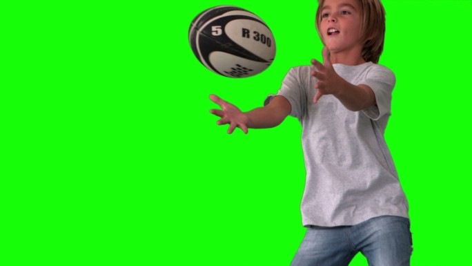 男孩跳起来抓住橄榄球在绿色屏幕近距离的慢动作
