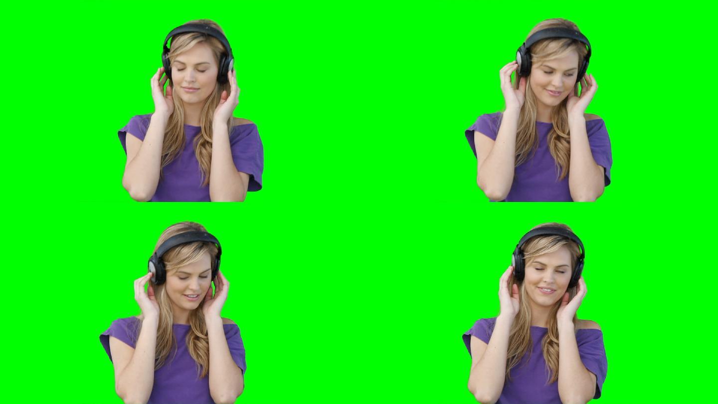 一个女人戴着耳机在绿色背景前随着音乐移动
