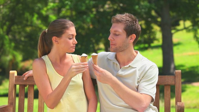 年轻的情侣们在公园的长椅上吃冰淇淋