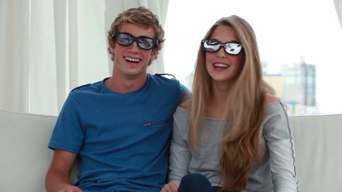 一对快乐的情侣戴着3D眼镜在客厅里玩