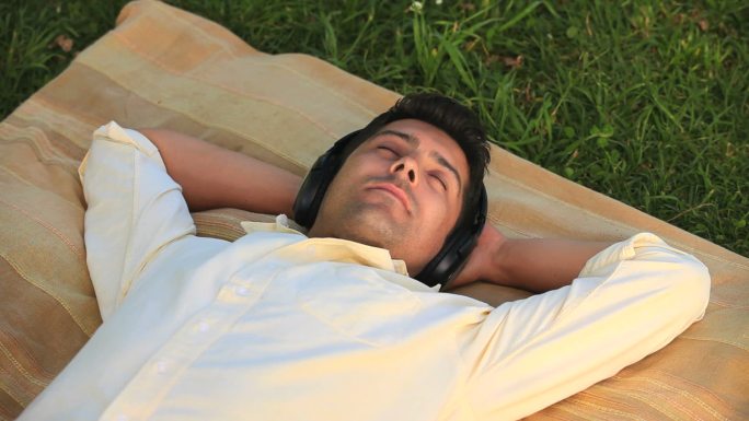 一个男人躺在草地上放松，戴着耳机听音乐