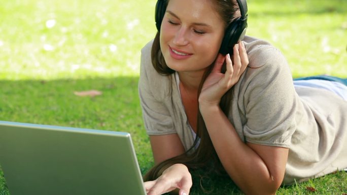 一个西方女性戴着耳机在笔记本电脑前趴着