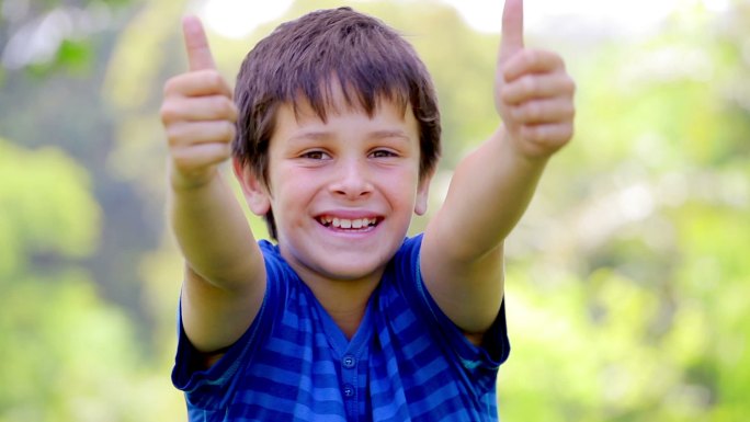 微笑的孩子在公园里竖起大拇指