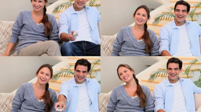 男人和女人坐在沙发上看电视，一边用电视遥控器一边笑