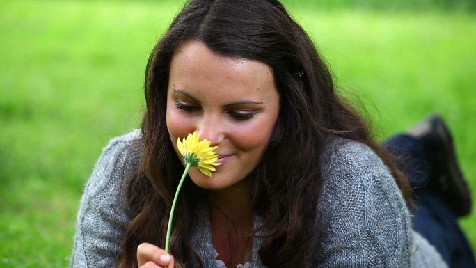 微笑的褐发女人闻着公园里的一朵黄花