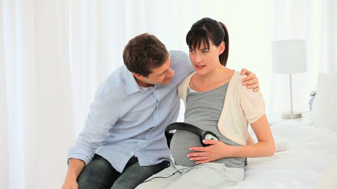 一对年轻夫妇让他们未来的宝宝在床上听音乐