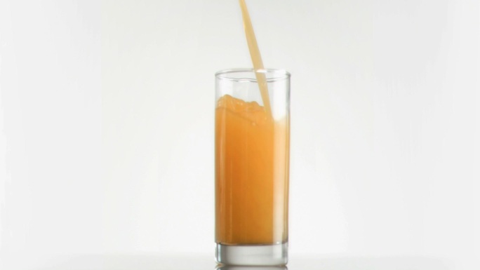 用超级慢镜头将芒果汁倒入白色背景的玻璃杯中