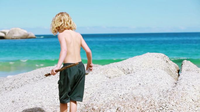 金发小孩在海滩上拿着一根木棍