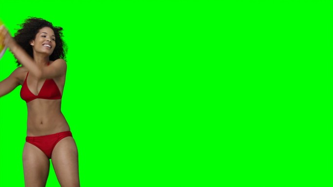 一个微笑的女人把一个沙滩球从屏幕上扔到绿色的背景上