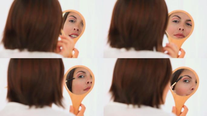 褐发女人在镜子上看着自己，孤立在白色的背景上