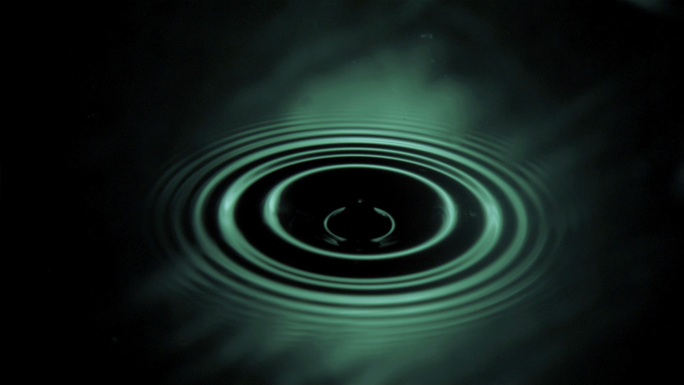在绿光下，水滴在水中以超慢的运动下落