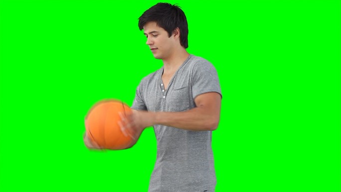 一个男人在绿色背景下练习用手指旋转篮球