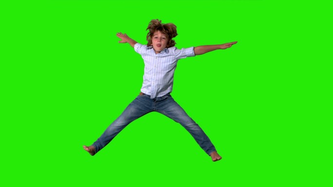 在绿色屏幕上，一个穿着衬衫和牛仔裤的小男孩跳了起来