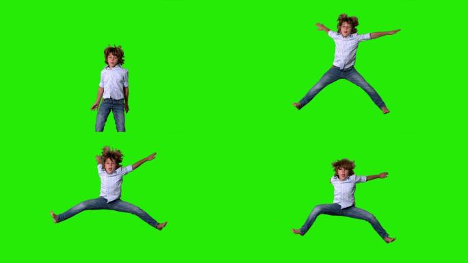 在绿色屏幕上，一个穿着衬衫和牛仔裤的小男孩跳了起来