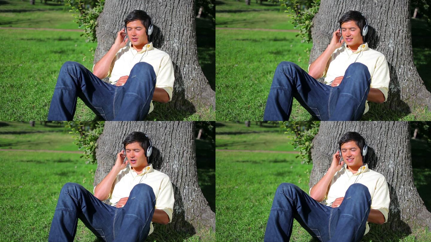 一个在公园里靠在树上听音乐的爱好和平的人