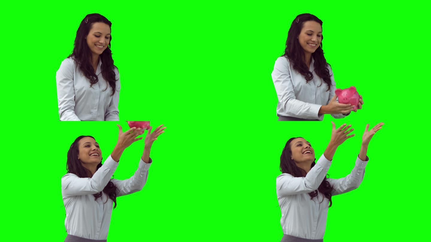 一个黑发女人在慢镜头中把一个存钱罐扔向绿色的背景