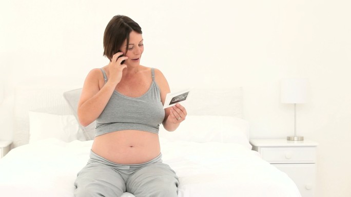 一名孕妇在床上打电话谈论她未来的孩子