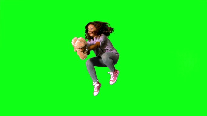 快乐的小女孩跳起来，在慢动作的绿色屏幕上抓住泰迪熊